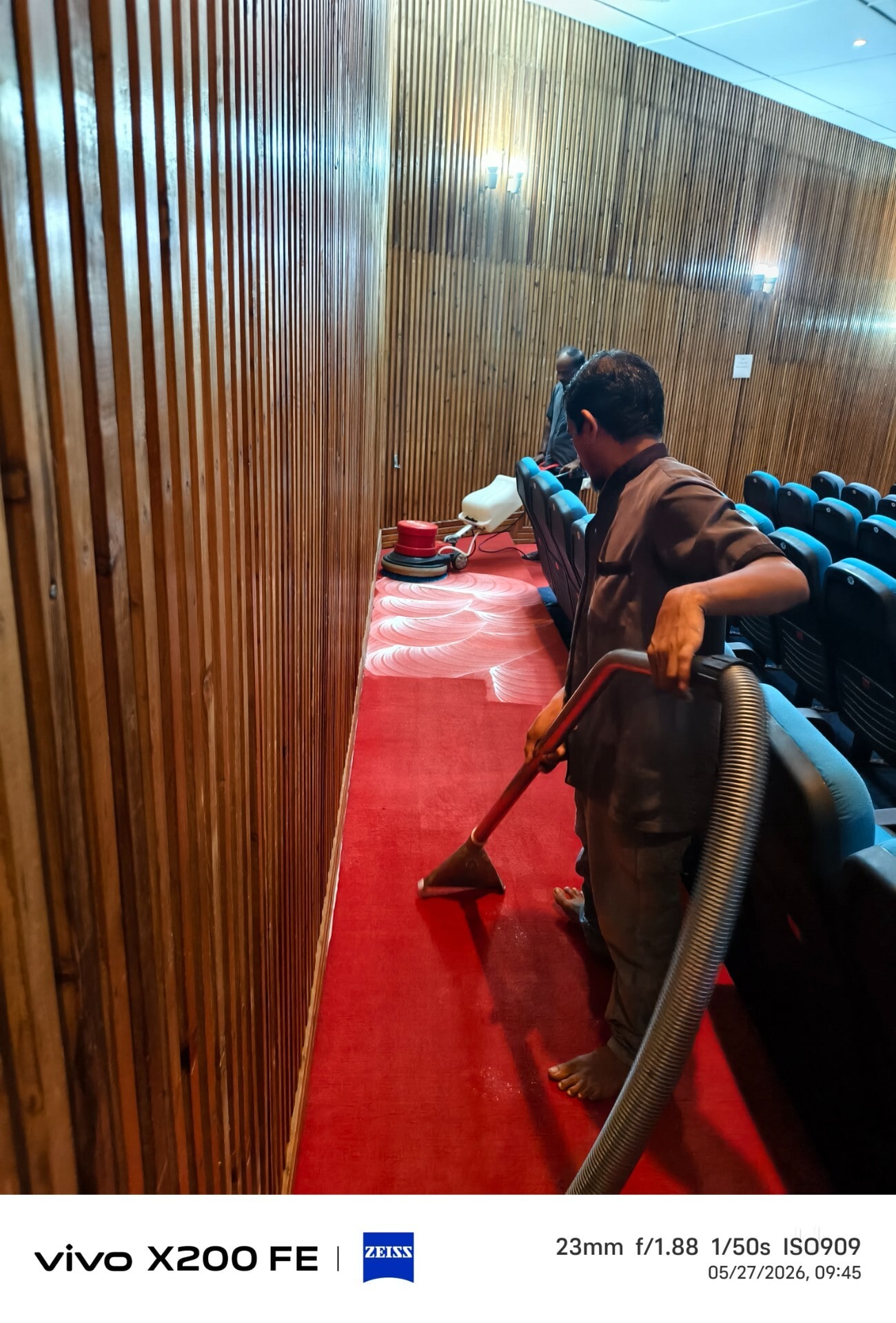 Worker vacuum-shampooing red carpet flooring inside an auditorium
